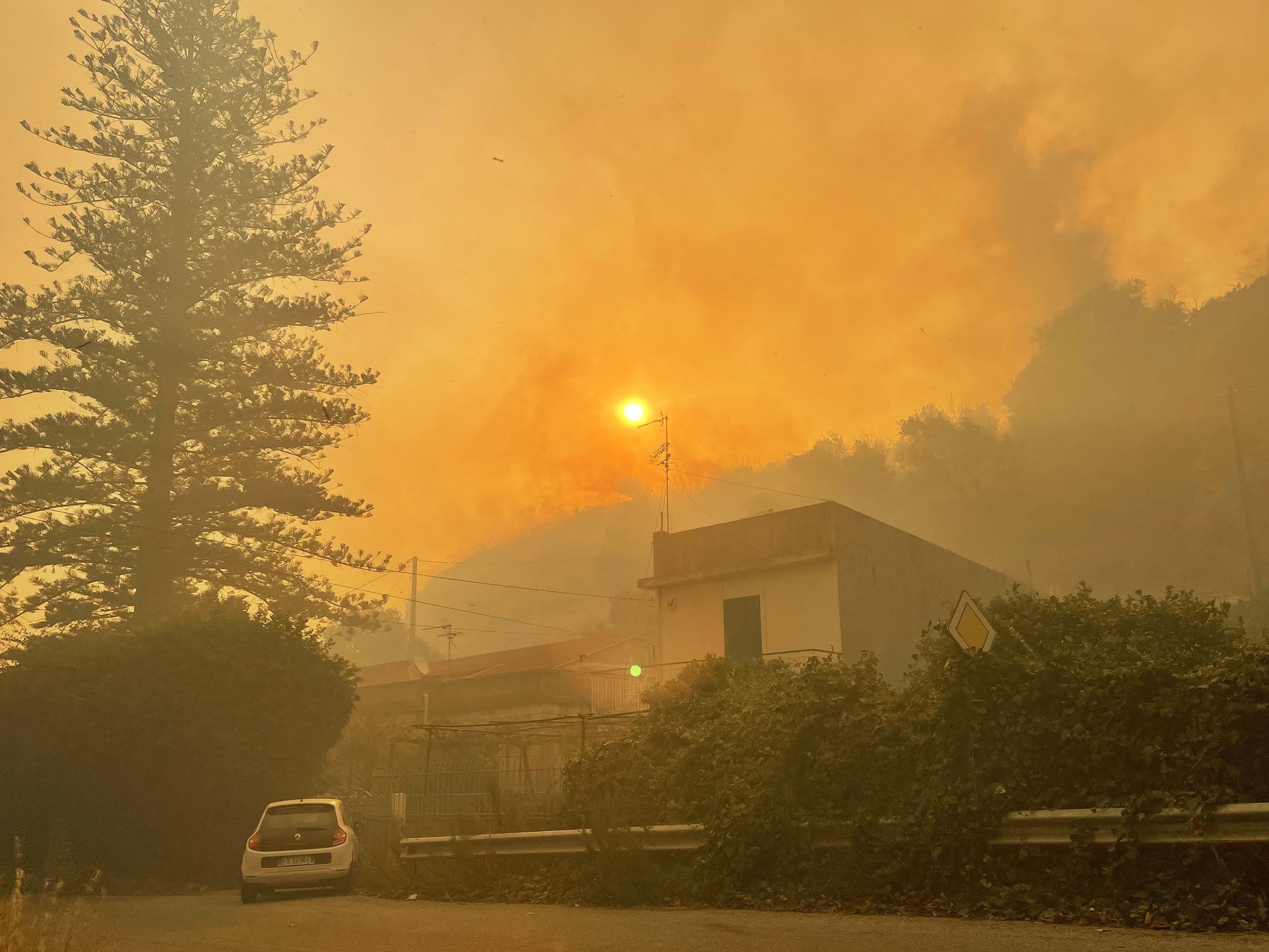 Foto yang diambil pada 26 Juli 2023 ini menunjukkan rumah-rumah di distrik Tono, Messina, Sisilia, saat api berkobar.