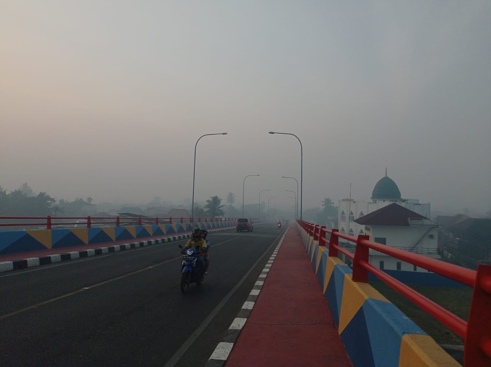 Pengendara roda dua saat hendak mengantar anaknya sekolah pada pagi hari di tengah kabut asap di Palembang.