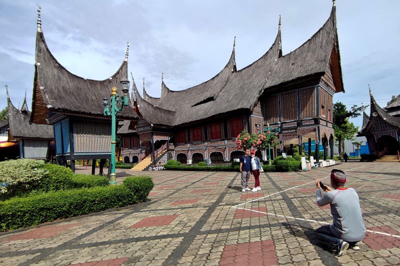 Pengunjung berfoto di belakang Rumah Gadang di anjungan Sumatera Barat di Taman Mini Indonesia Indah (TMII).