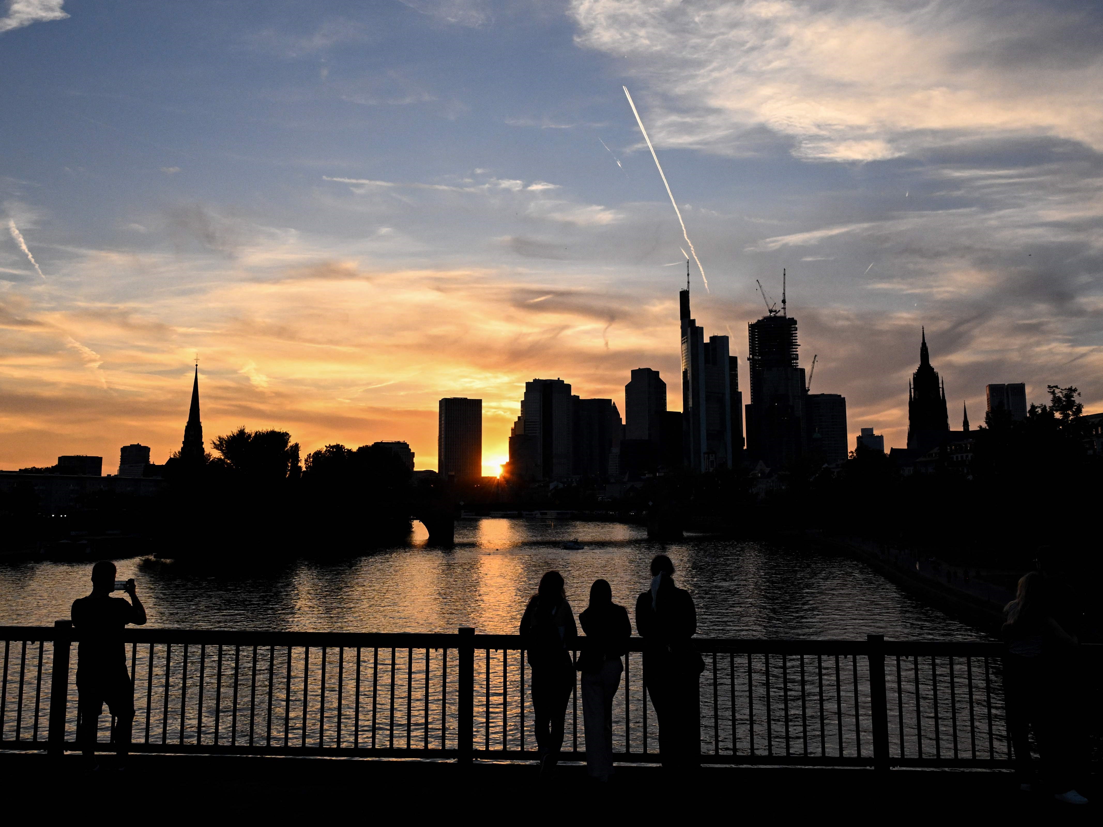 Orang-orang melihat cakrawala distrik perbankan dengan gedung Commerzbank saat matahari terbenam di Frankfurt am Main, Jerman barat.