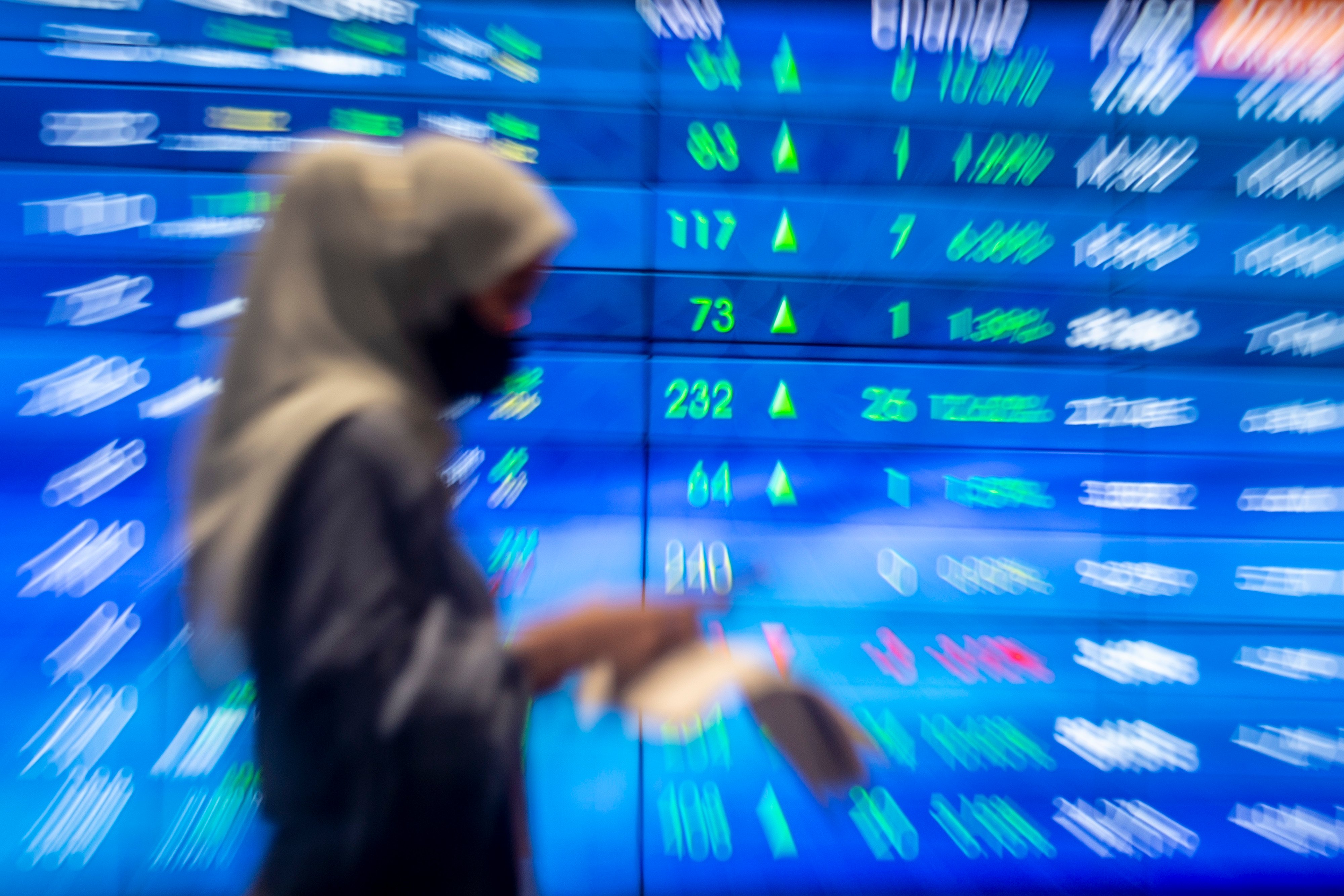 Pekerja berjalan dengan latar belakang layar pergerakan harga saham di gedung Bursa Efek Indonesia, Jakarta, Jumat (8/4/2022)