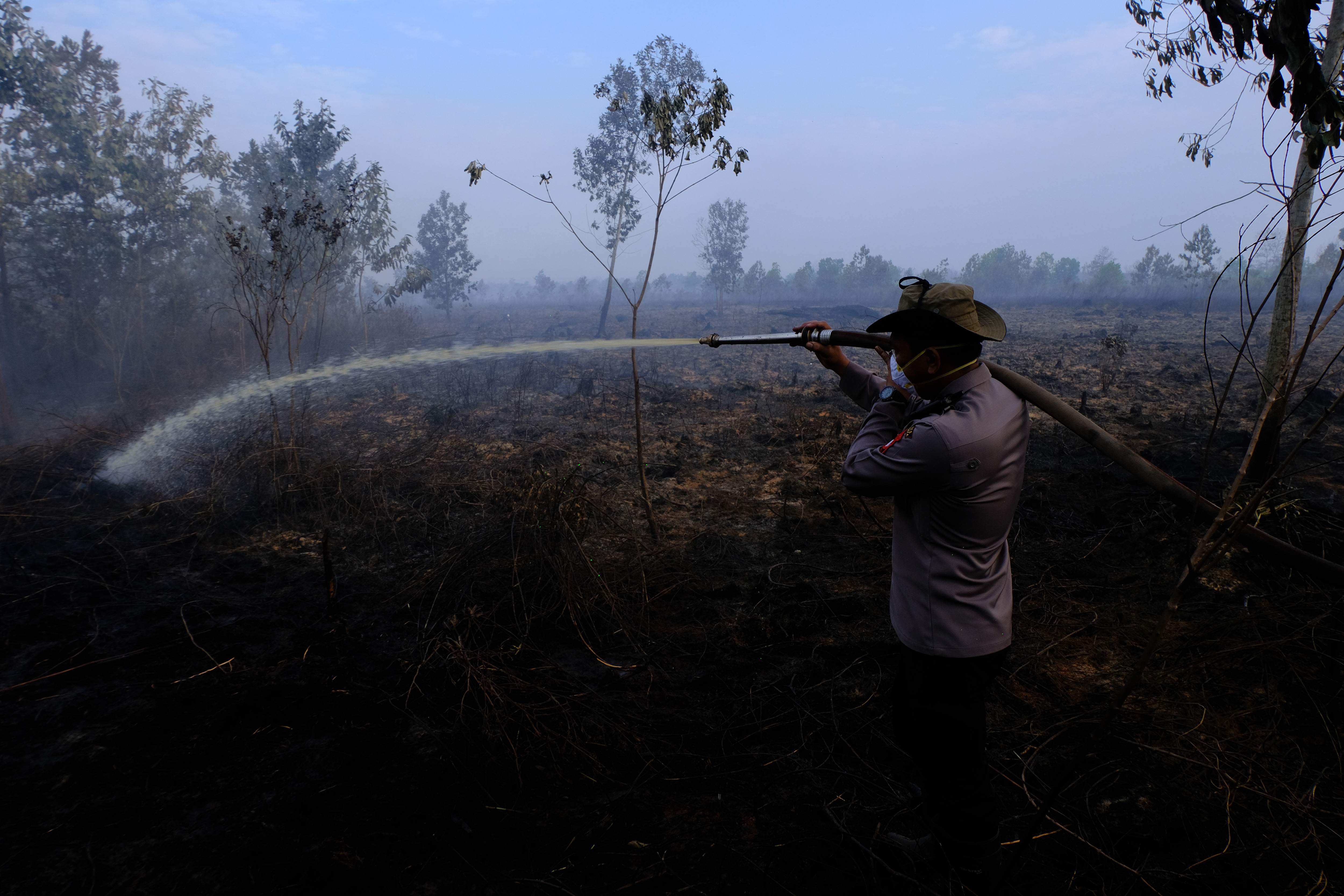 Petugas kepolisian melakukan pembasahan di lokasi kebakaran lahan gambut 