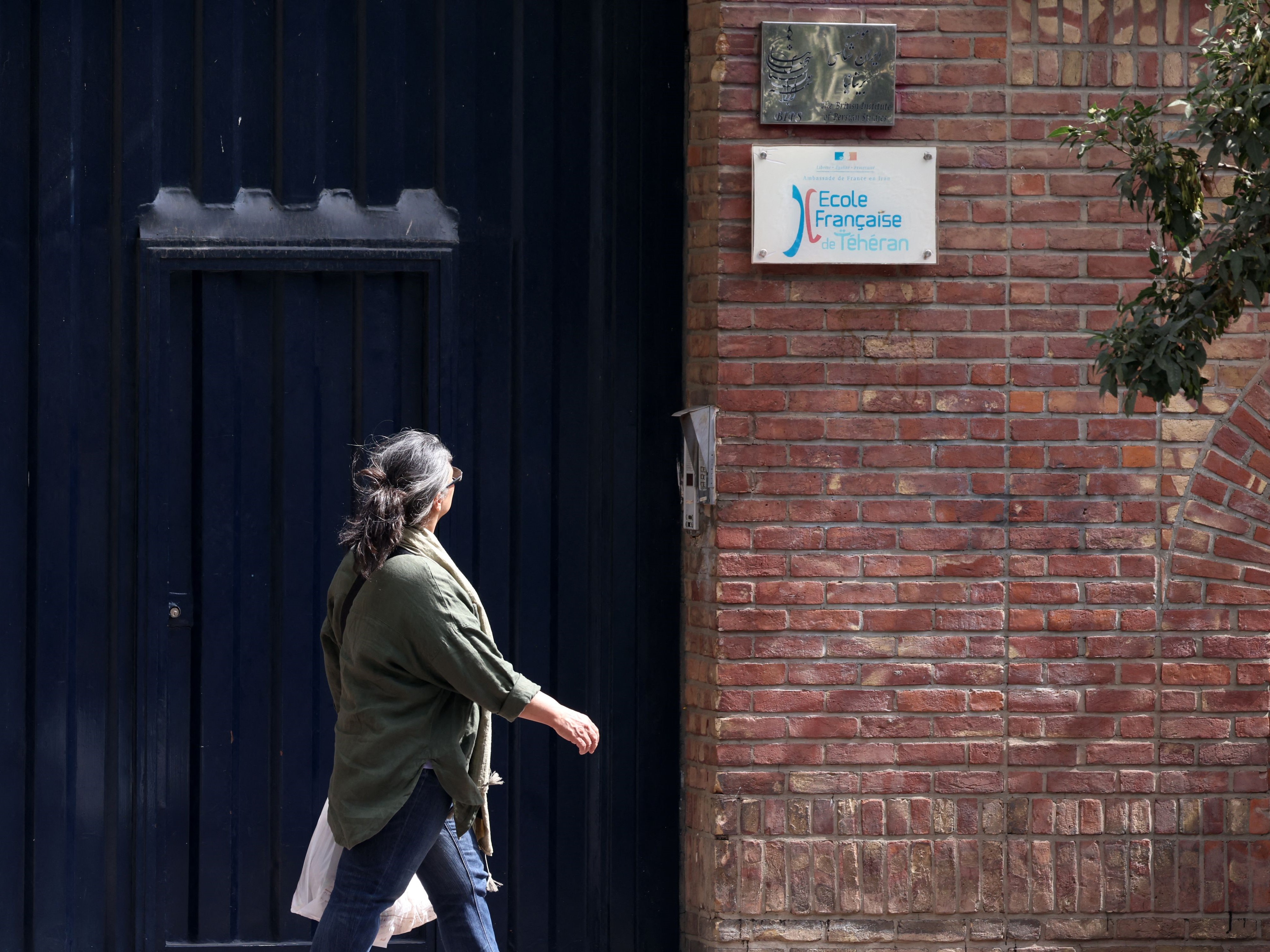 Seorang wanita melihat papan nama saat dia berjalan di depan sekolah Prancis di Teheran utara pada 3 Oktober 2023.