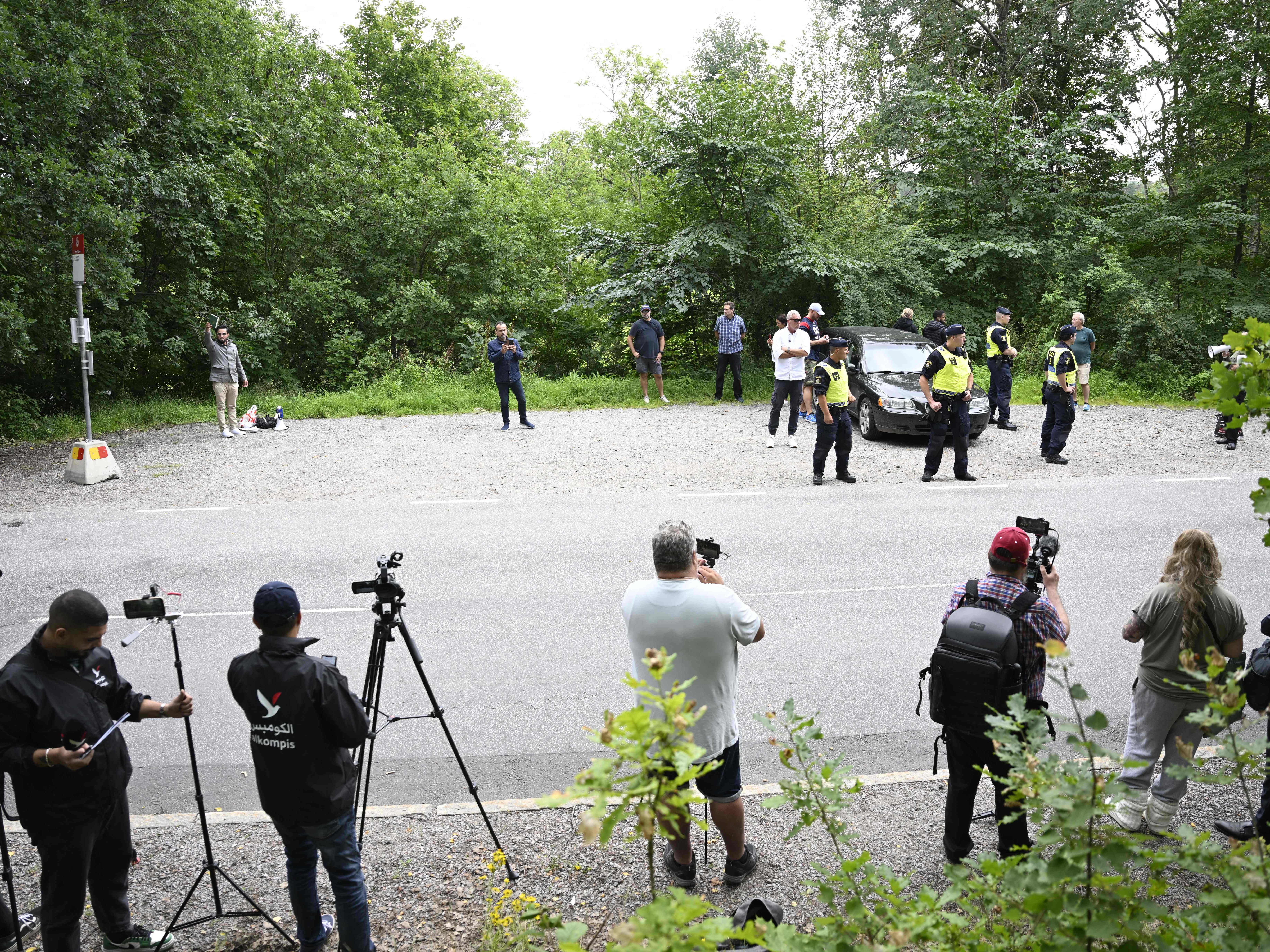 Pengungsi Irak di Swedia Salwan Momika (belakang, kiri) memegang Al-Qur'an ketika polisi dan jurnalis berdiri di sekelilingnya.