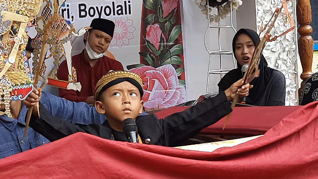 Seorang dalang bocah memperagakan adegan panggung wayang kulit.