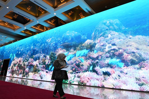 Seorang wanita berjalan melintasi monitor yang menampilkan ekosistem laut di lokasi KTT AIS Forum 2023, Bali Nusa Dua Convention Center.