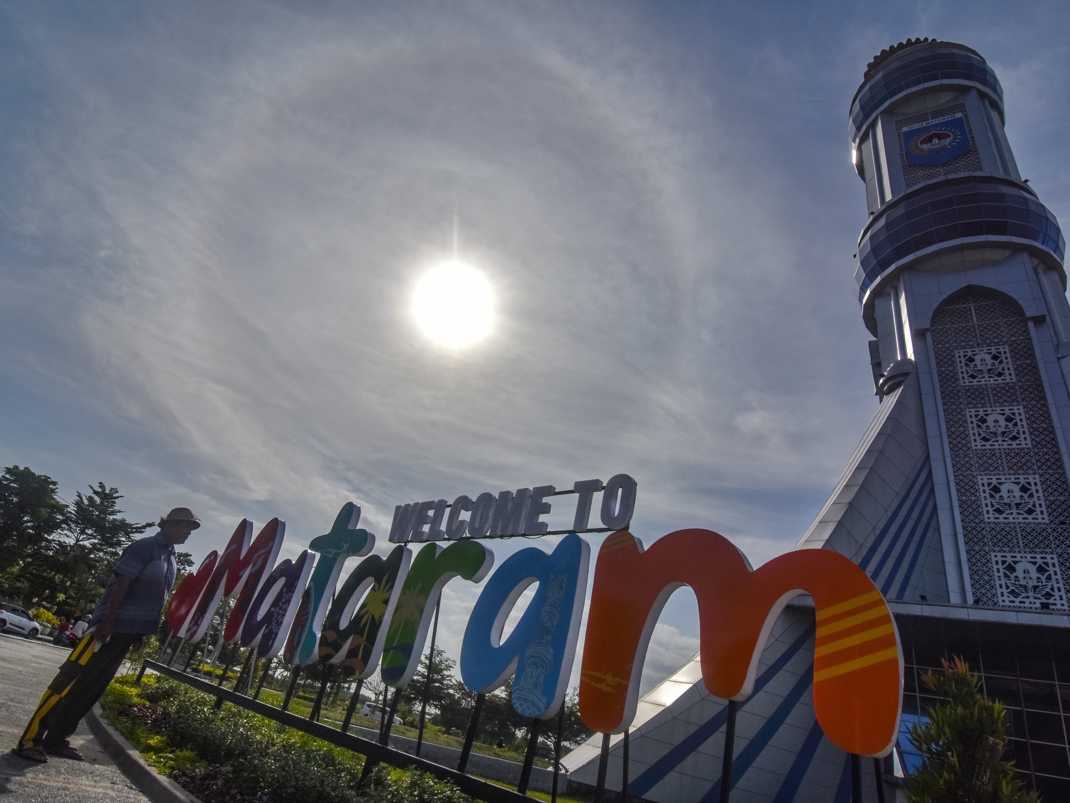 Seorang laki-laki berdiri di areal tugu Mataram Metro dengan latar belakang Halo Matahari di Mataram, NTB, Selasa (19/7/2022).