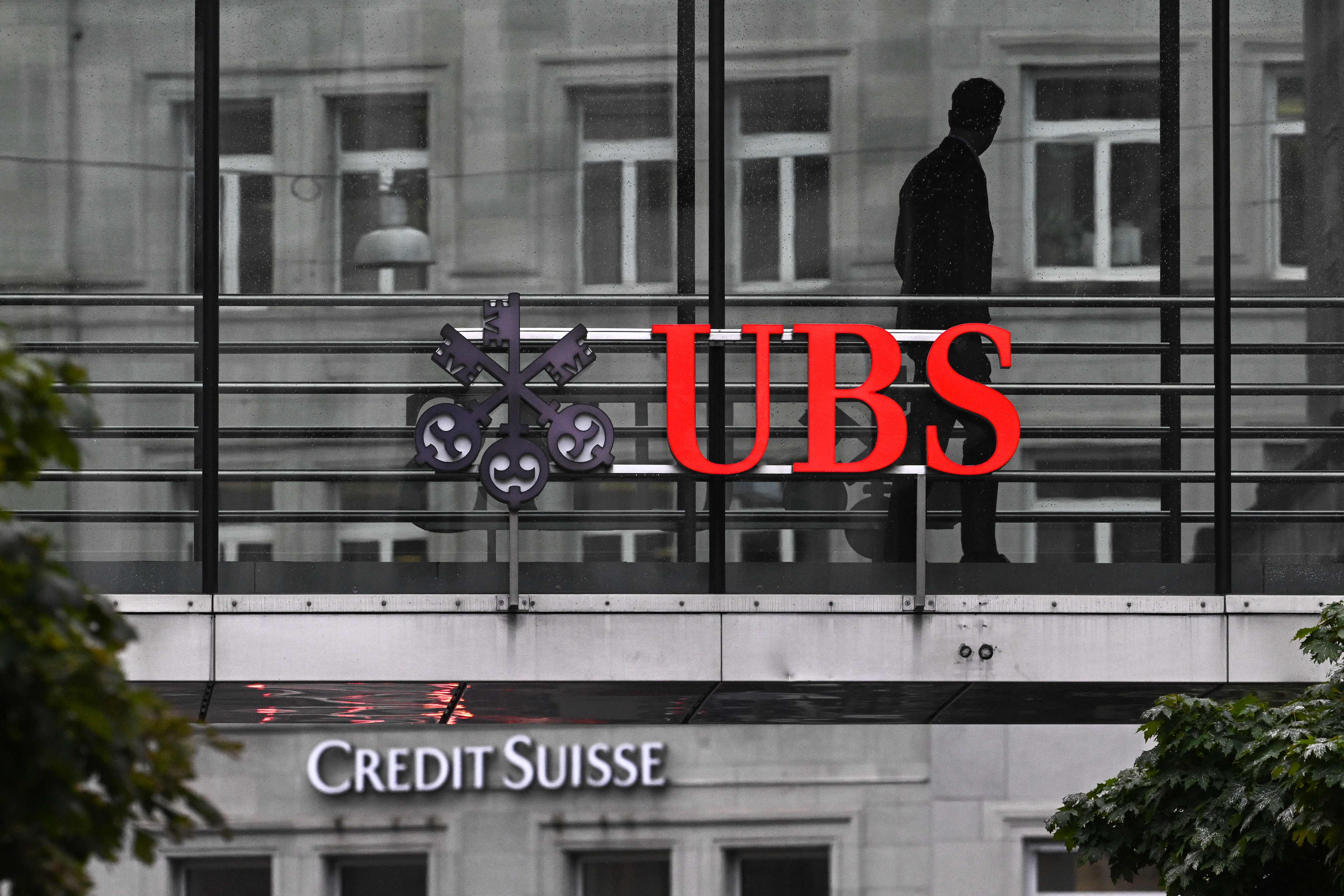 Seorang pegawai berjalan melewati papan nama perbankan raksasa Swiss UBS dan Credit Suisse di Zurich