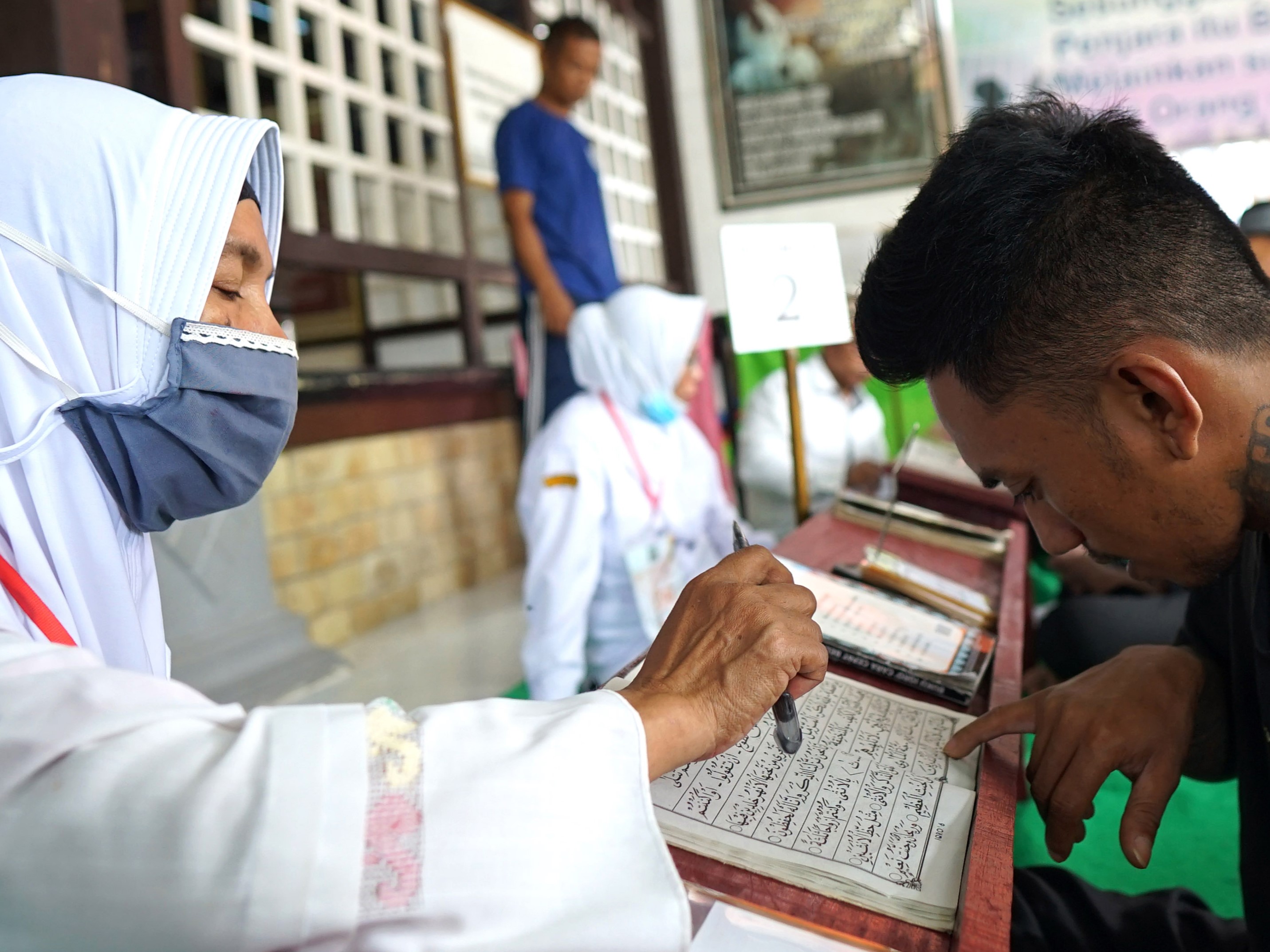 Seorang warga binaan pemasyarakatan didampingi penyuluh agama belajar mengaji di pelataran Masjid At-Taubah dalam LP.