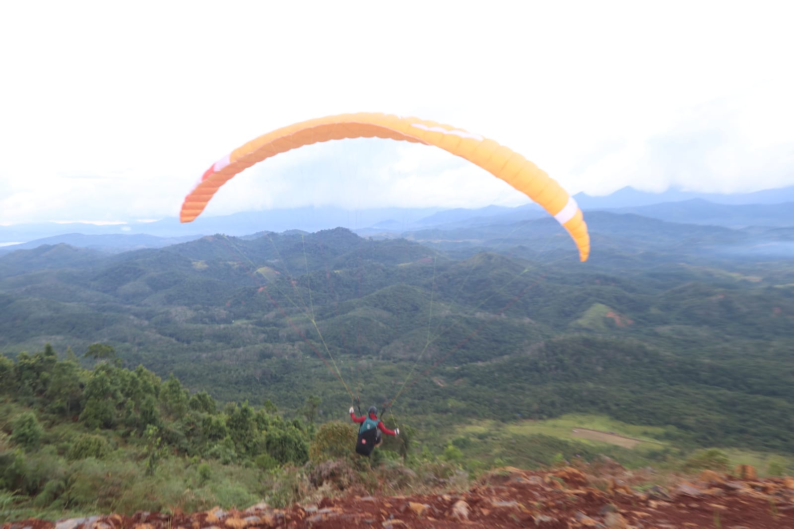 Seorang warga tengah menikmati pemandangan dari ketinggian menggunakan paralayang