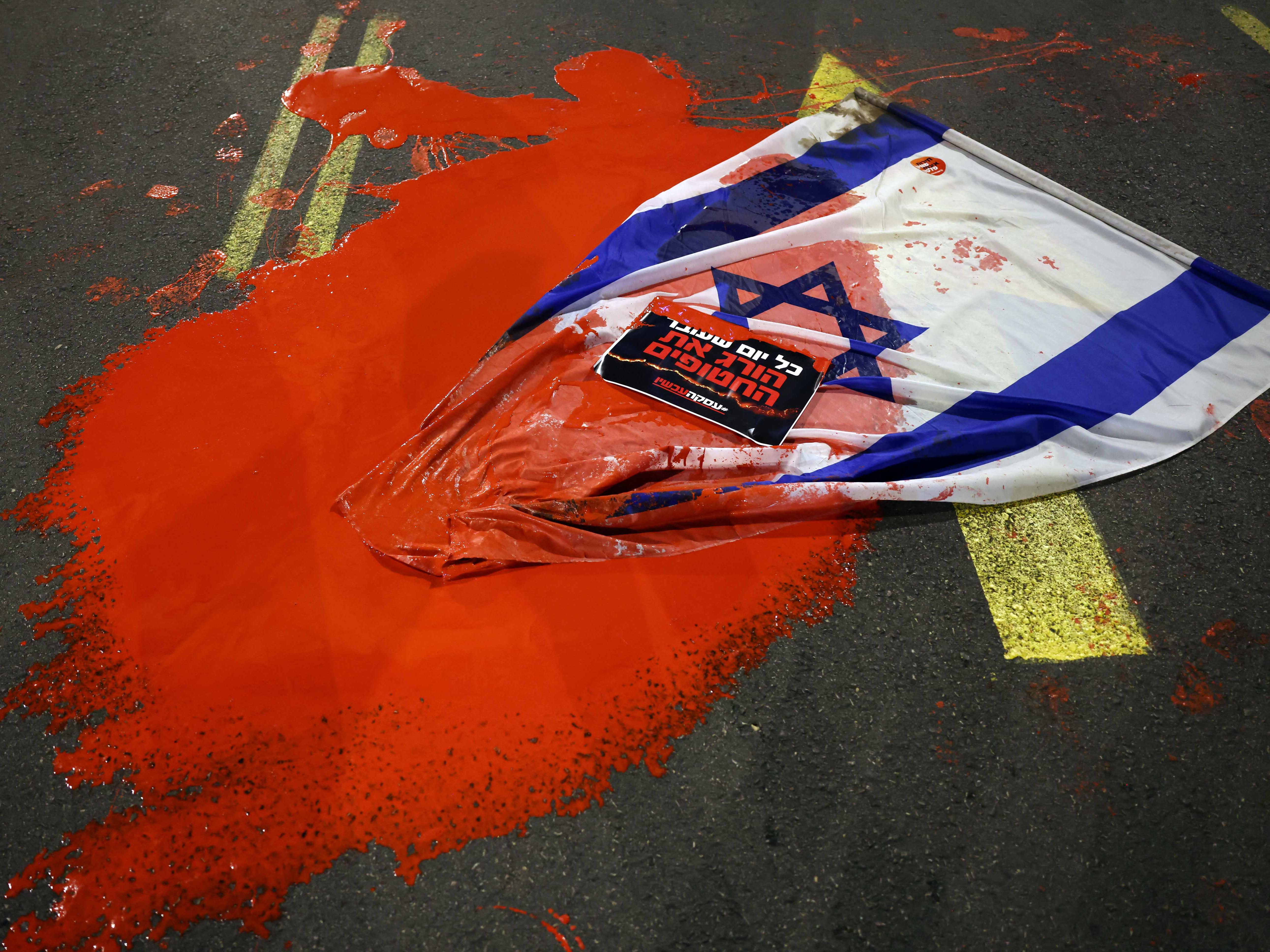 Bendera Israel ditutupi cat merah ketika kerabat dan pendukung sandera berdemonstrasi di luar Kemenhan Israel.
