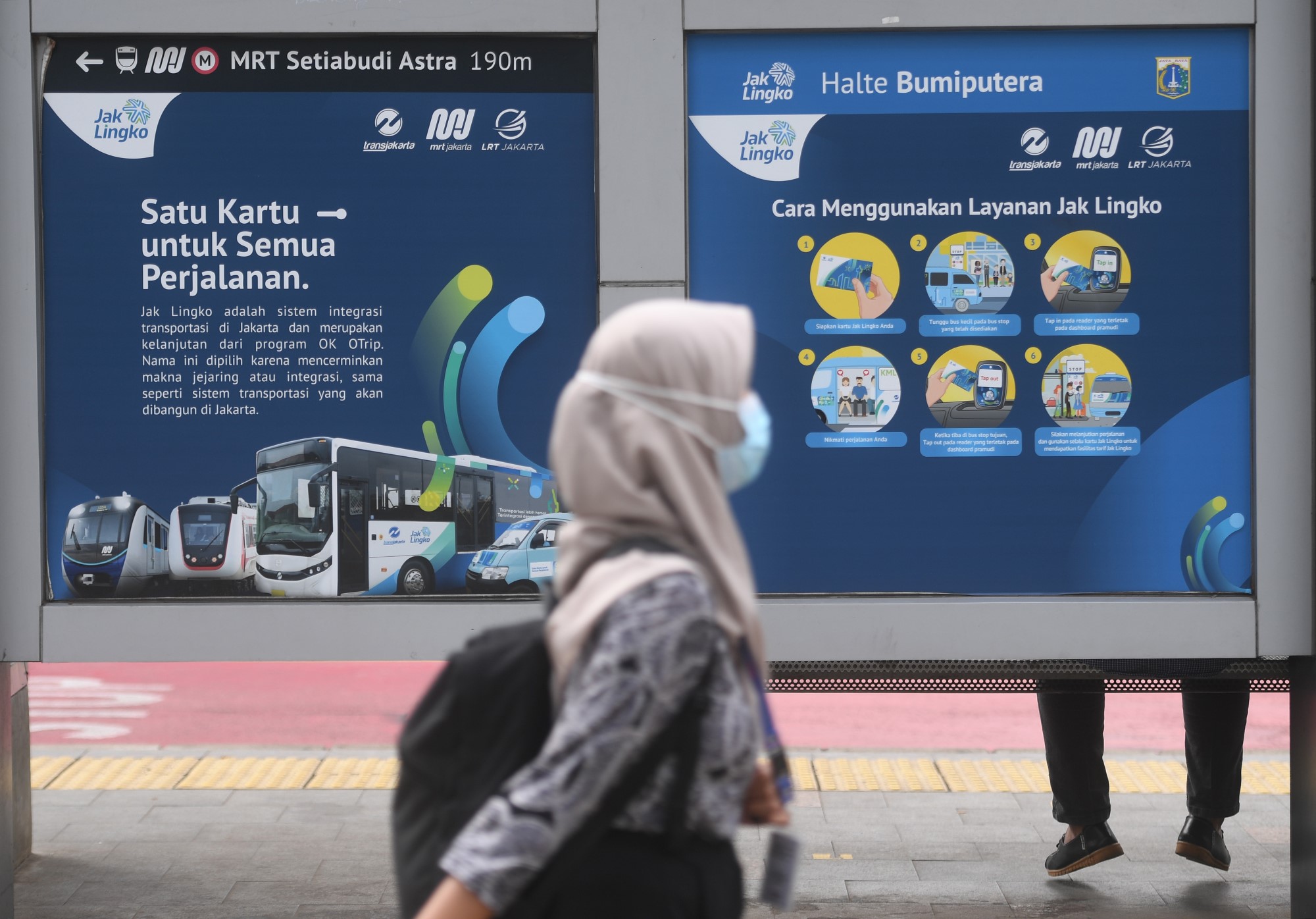 Warga berjalan di depan papan informasi mengenai JakLingko