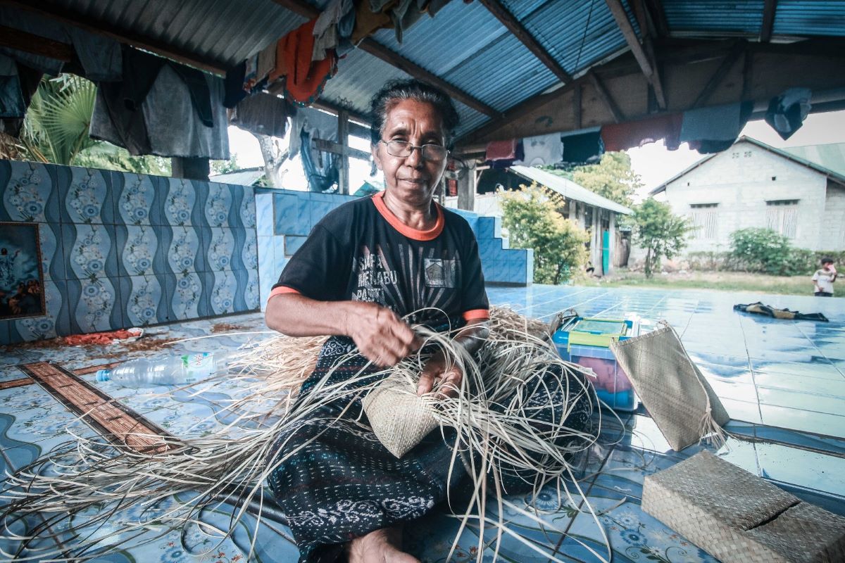 Lusia sedang duduk menganyam di atas kuburan suaminya.