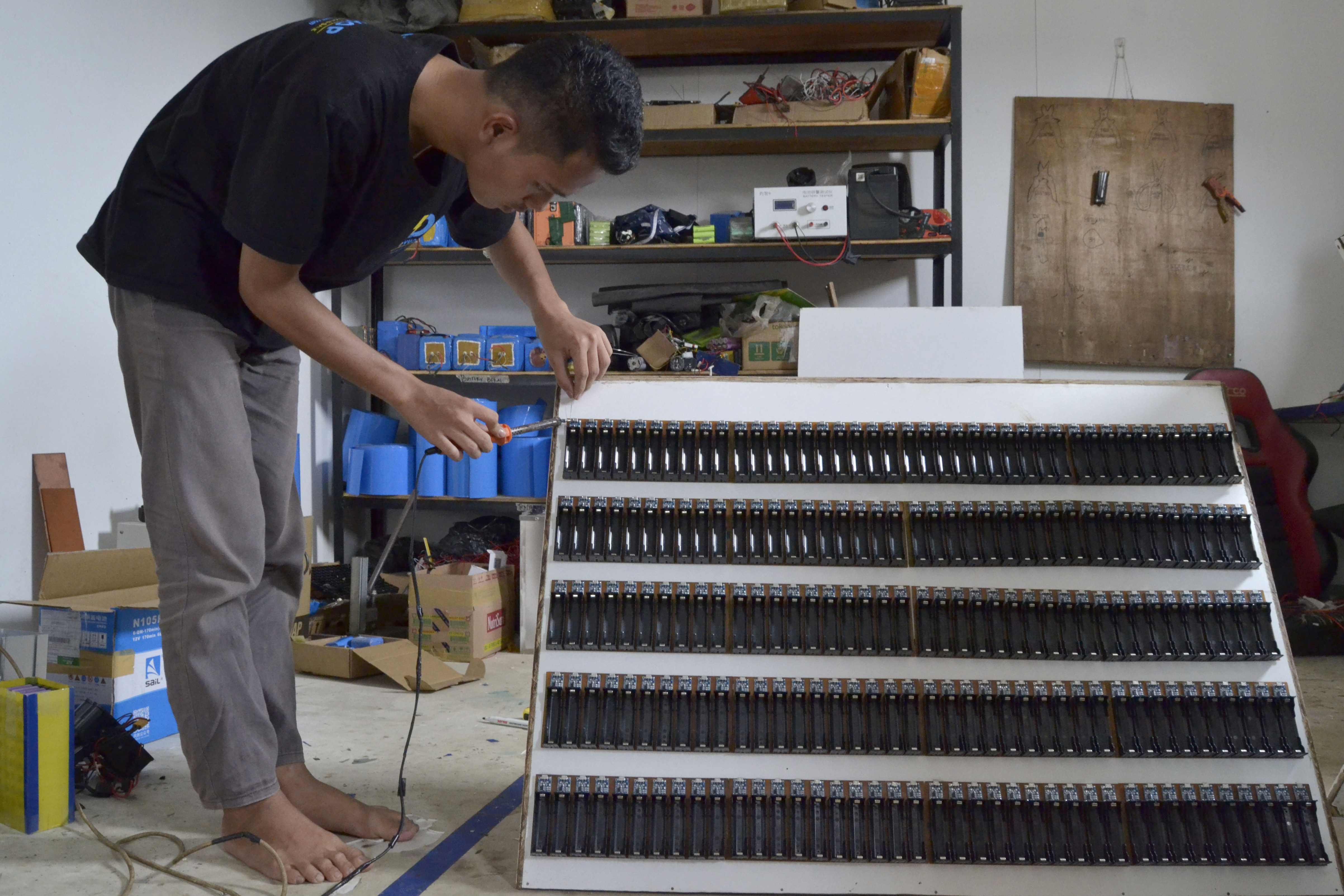 Seorang teknisi merakit rak pengisian ulang baterai motor listrik di bengkel motor listrik