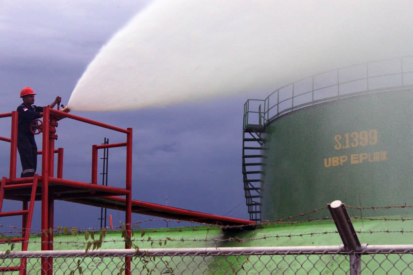 Pekerja sedang melakukan penyiraman air untuk pendinginan tangki penampung minyak mentah 