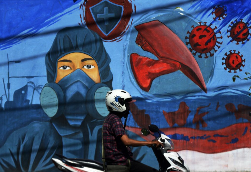 Pengendara melintas di depan mural bertema covid-19 di kawasan Jalan Nusantara, Makassar, Sulawesi Selatan, Senin (1/11/2021)