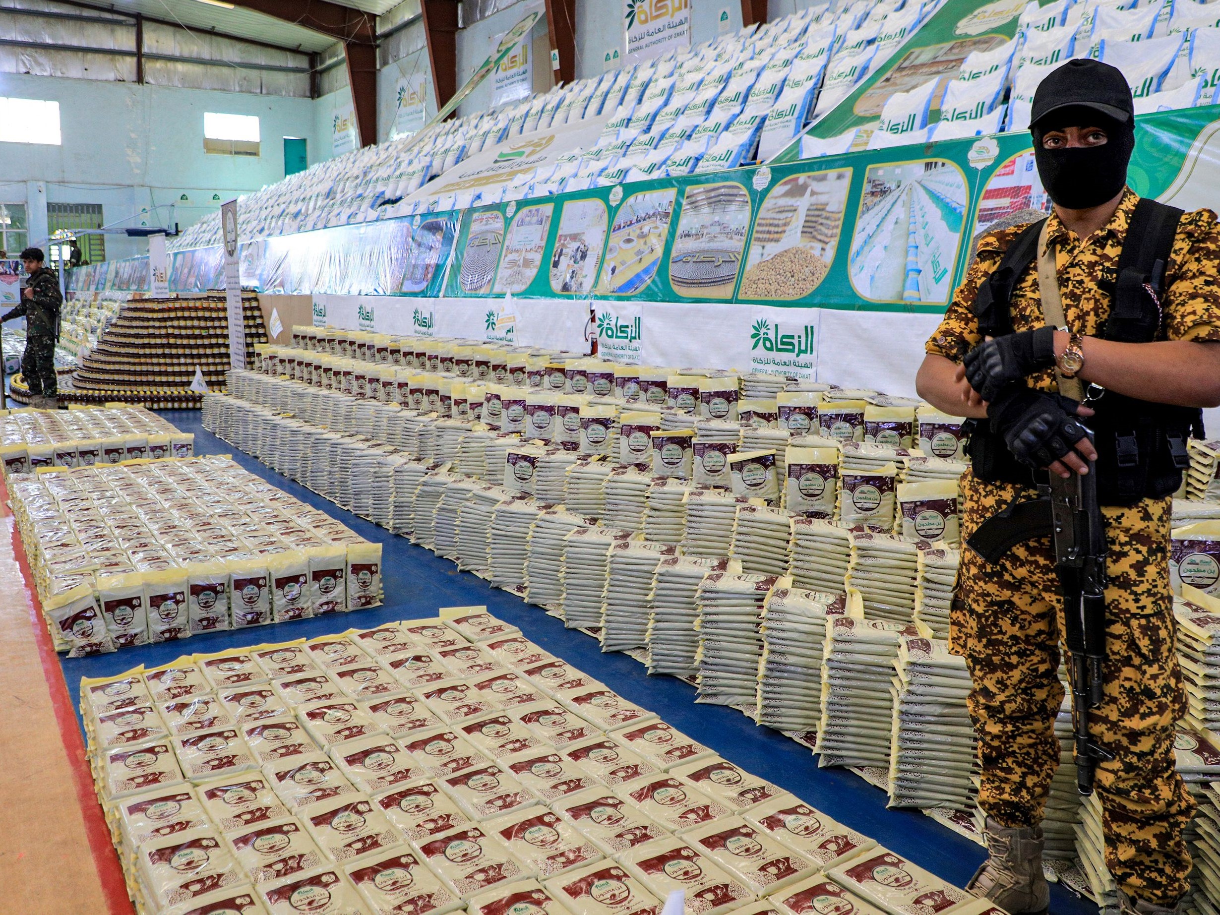 Seorang penjaga keamanan Yaman berdiri di samping persediaan makanan yang disediakan oleh otoritas amal zakat yang dikelola Huthi.