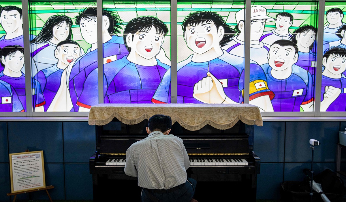 Seorang warga berman piano di depan kaca yang menampilkan karakter Captain Tsubasa di stasiun kereta Urawa-Misono di Saitama, Jepang.