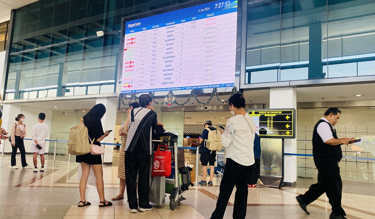 penumpang memperhatikan papan informasi penerbangan di Bandara Internasional Juanda