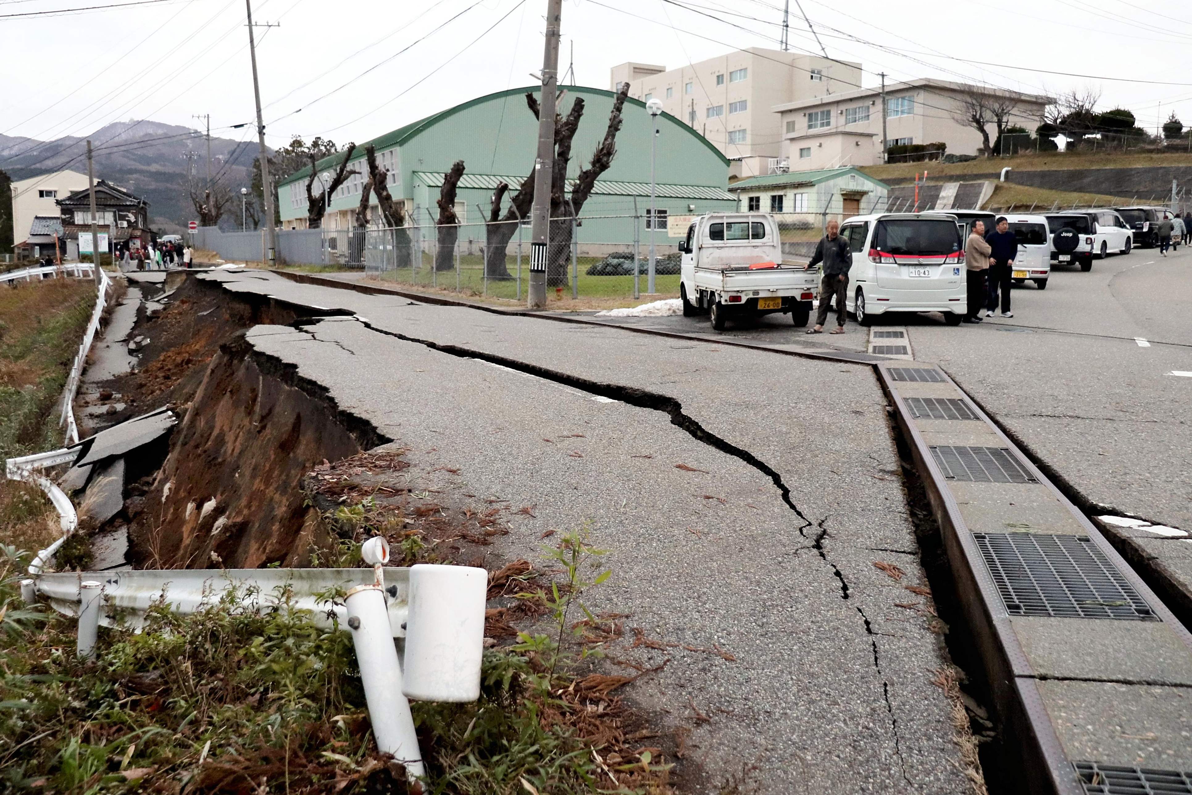 Warga berdiri di dekat retakan besar di trotoar jalan di kota Wajima, prefektur Ishikawa, pada Senin (1/1/2024) setelah gempa Magnitudo 7,6 