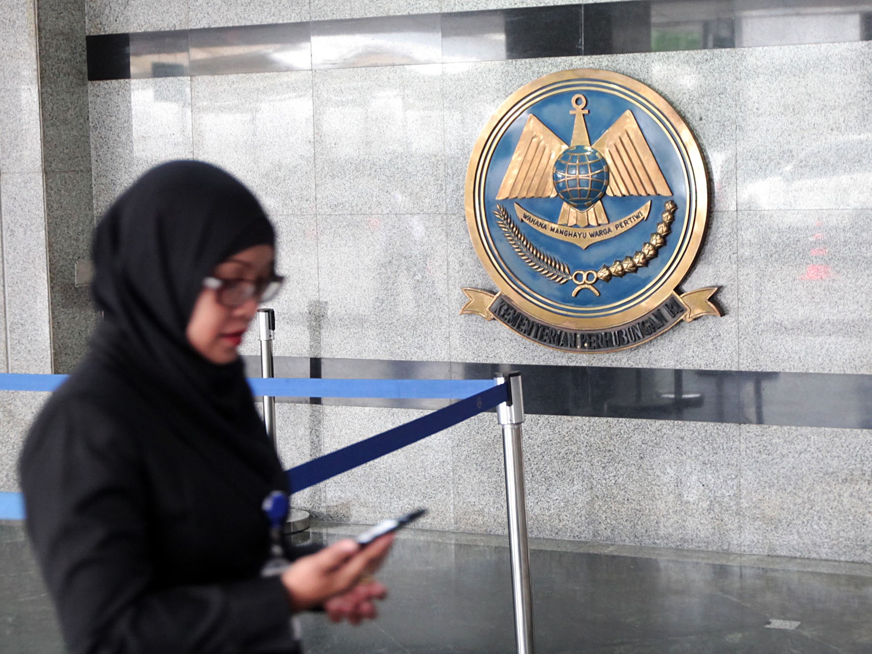 Seorang wanita berdiri berlatarkan logo Kementerian Perhubungan (Kemenhub), Jakarta, Kamis (13/10).
