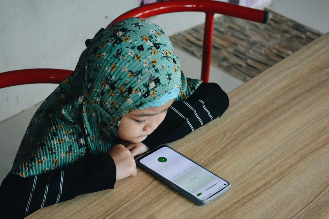 Seorang anak perempuan menggunakan aplikasi ngaji.ai di ponsel pintar.