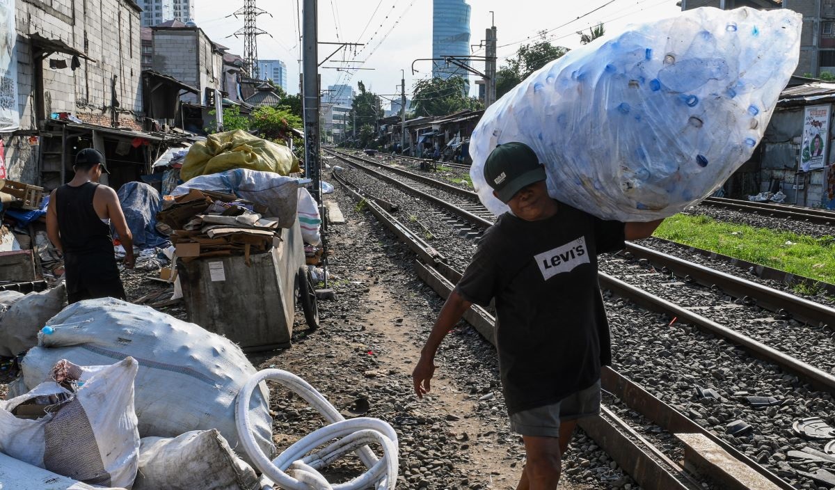Pemulung memikul botol plastik di area perlintasan kereta api Palmerah-Tanah Abang, Jakarta, Jumat (5/1/2024).