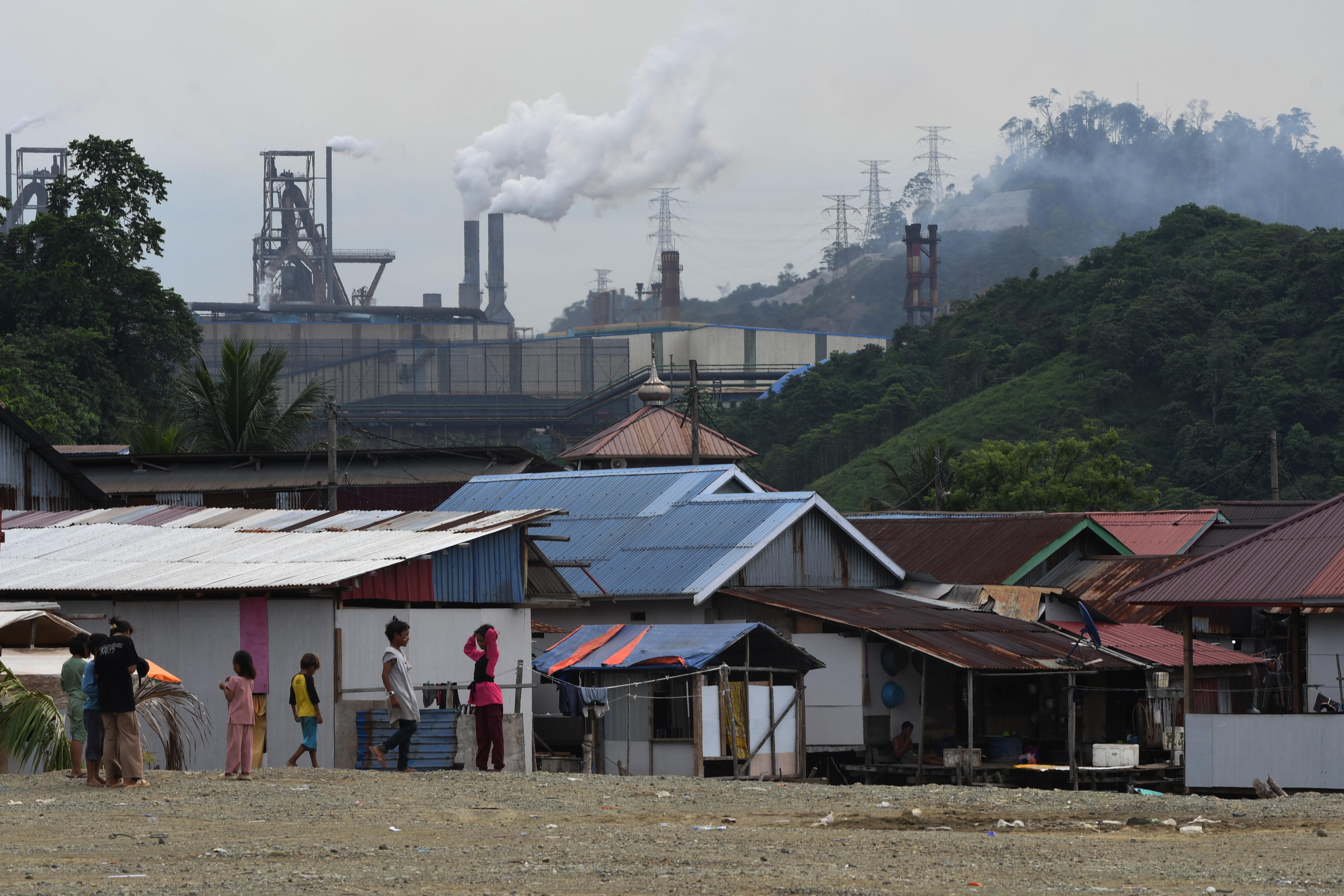 Anak-anak bermain di sekitar pemukiman mereka dengan latar belakang aktivitas industri nikel PT Indonesia Morowali Industrial Park