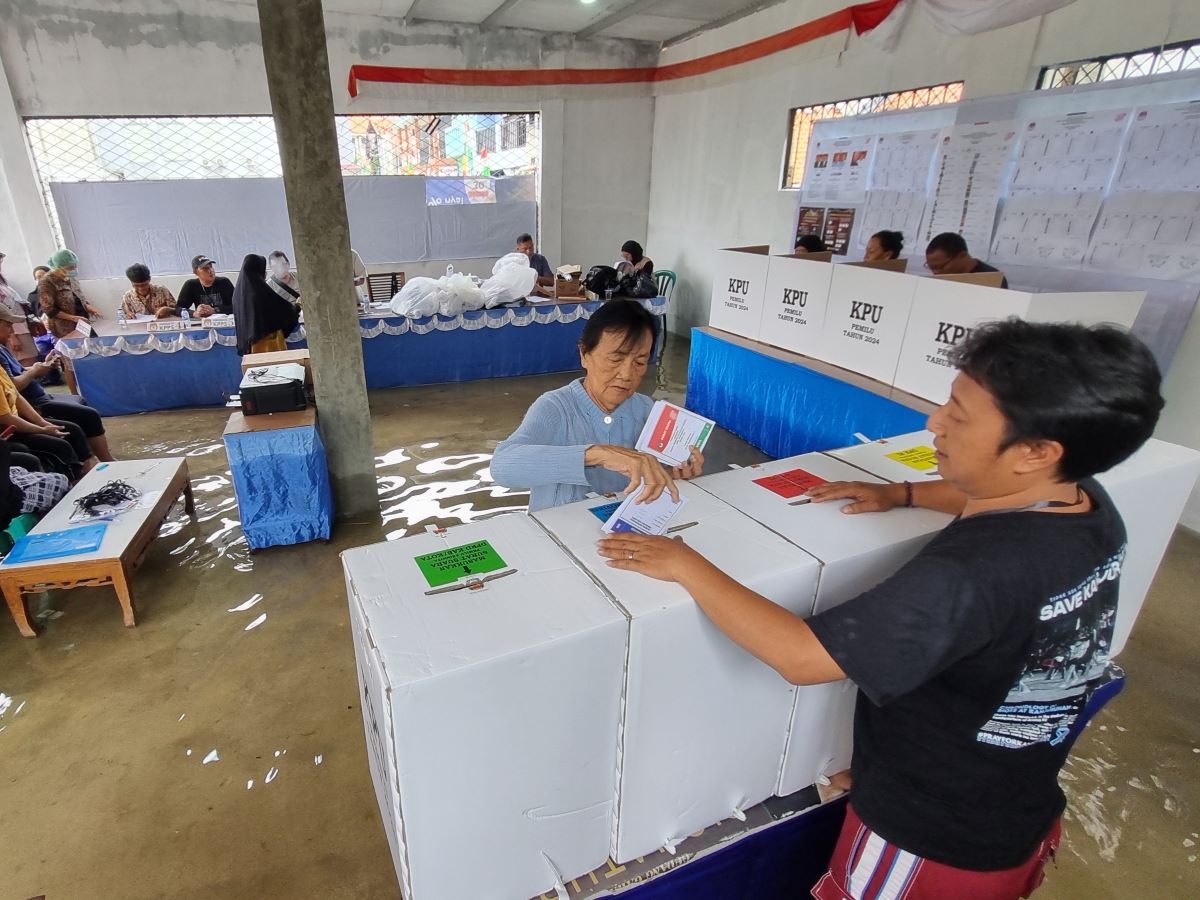 Warga memasukkan surat suara ke dalam kotak setelah melakukan pencoblosan di TPS 20 RT.01/05 yang tergenang banjir di Larangan Utara.