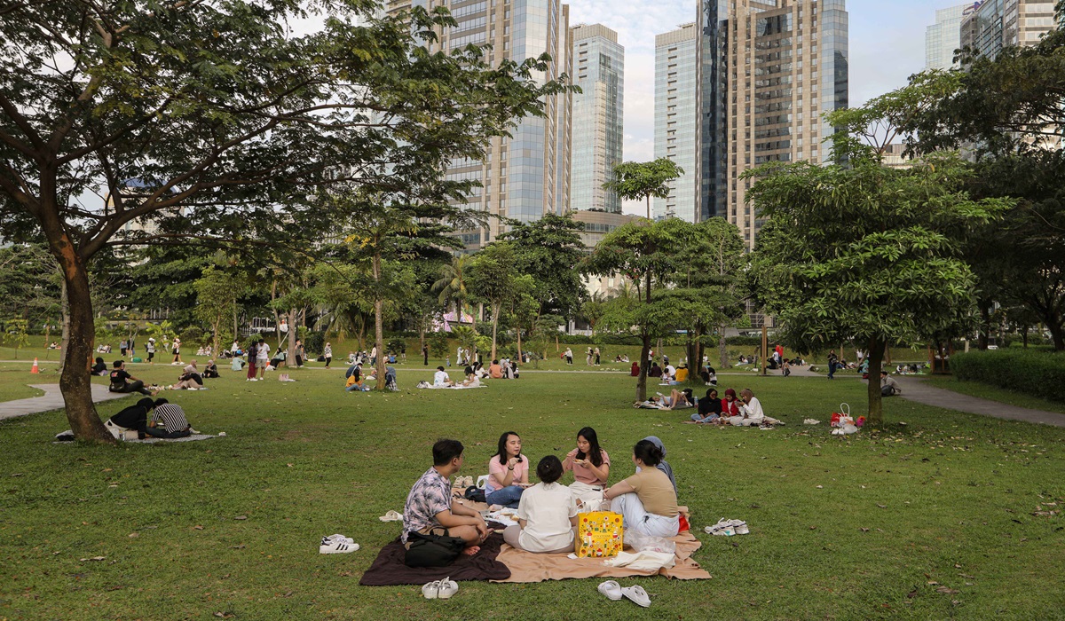 Warga mendatangi taman kota untuk menikmati sore dengan pemandangan gedung bertingkat Kota Jakarta di Hutan Kota, Jakarta.
