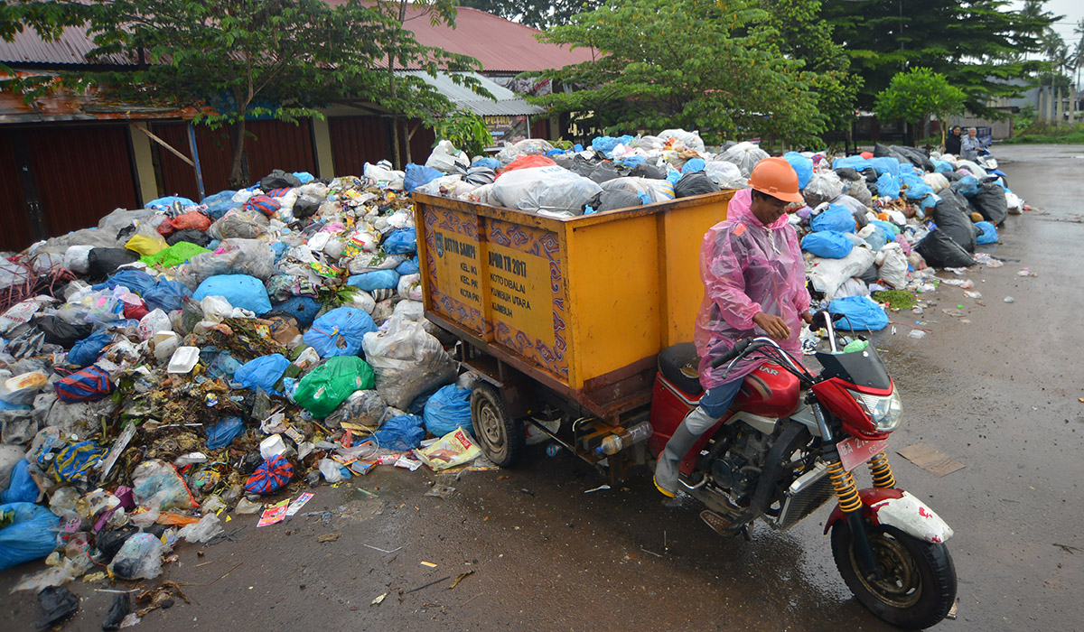 Pekerja membuang sampah di tempat pembuangan sampah sementara yang sudah menggunung di Pasar Padang Kaduduak, Kota Payakumbuh.
