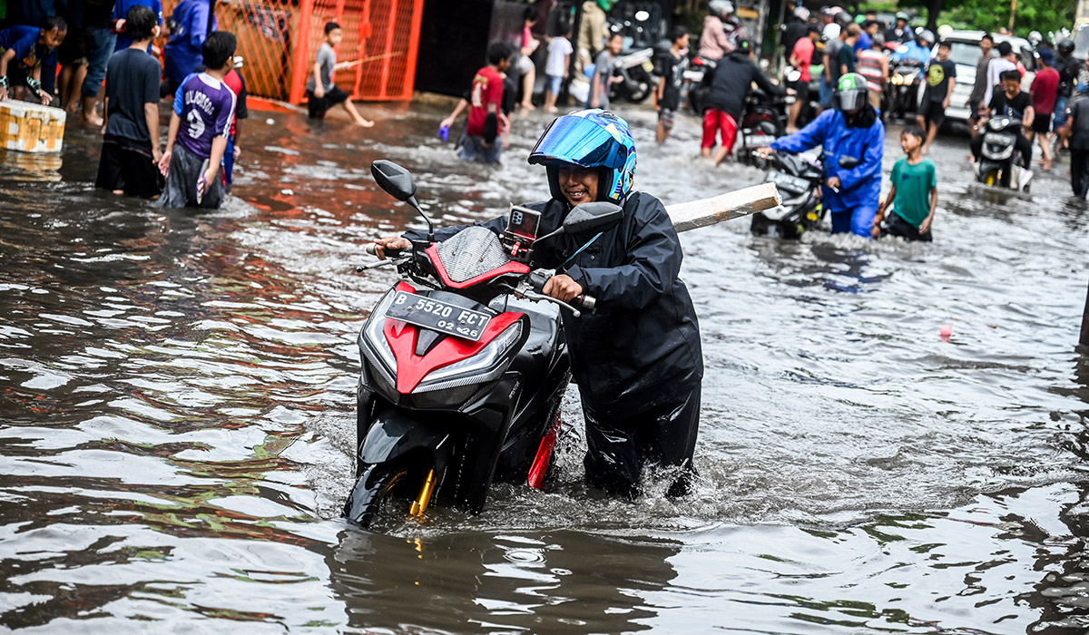 Pengendara mendorong motornya saat melintasi banjir di kawasan Joglo, Jakarta, Jumat (22/3).