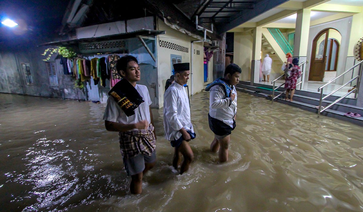 Jemaah berjalan melintasi genangan air banjir akibat luapan Sungai Bengawan Solo saat hendak salat tarawih di Bojonegoro.