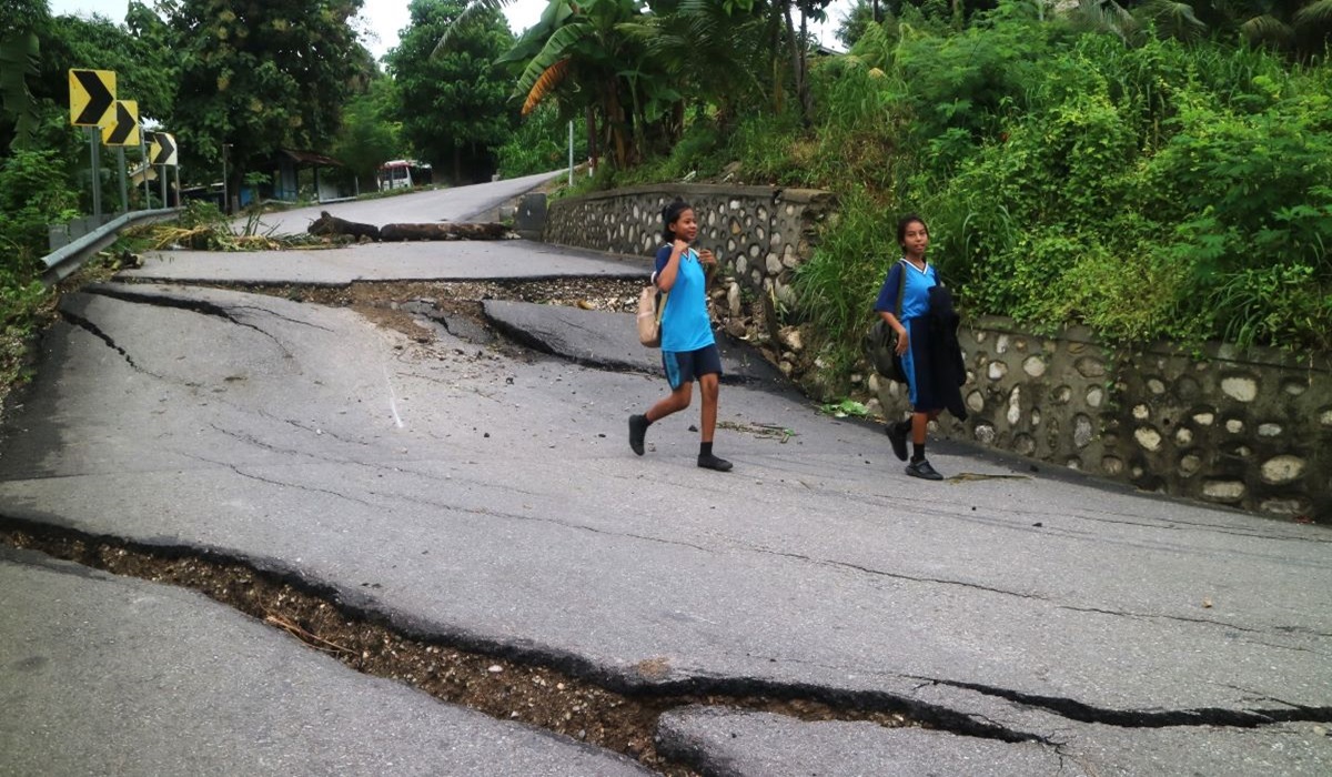 Dua siswi melintasi Jalan Taebenu di Kota Kupang, NTT yang ambles sejak Selasa (12/3) akibat cuaca ekstrem.