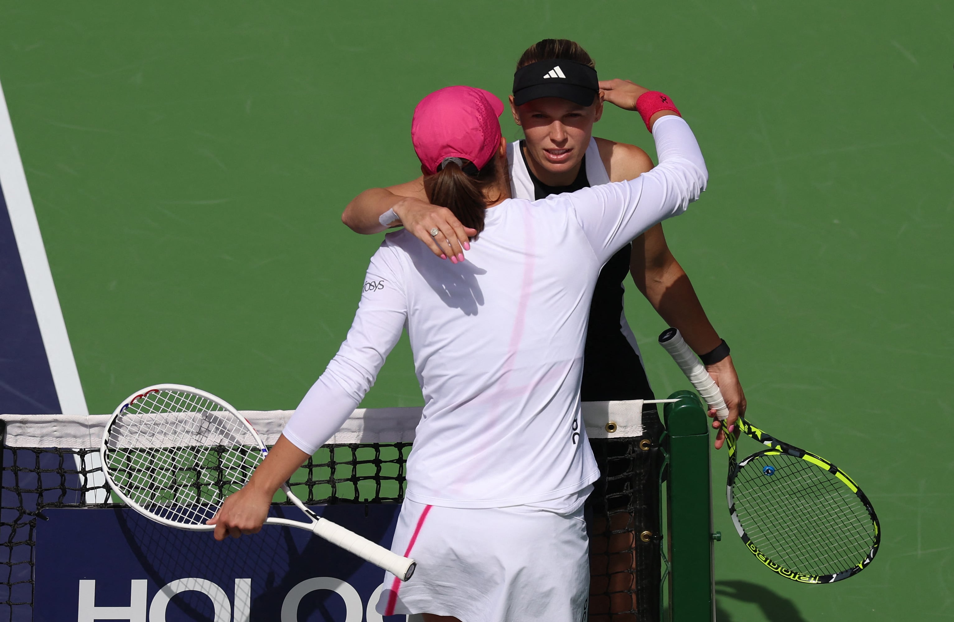 Iga Swiatek (topi hitam) memeluk lawannya Caroline Wozniacki seusai laga perempat final Indian Wells, Jumat (15/3)