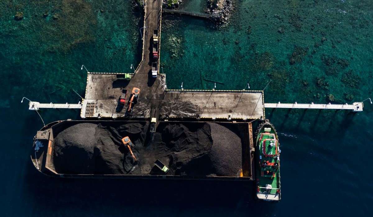 Foto udara pekerja mengoperasikan alat berat saat bongkar muat batu bara ke dalam truk 