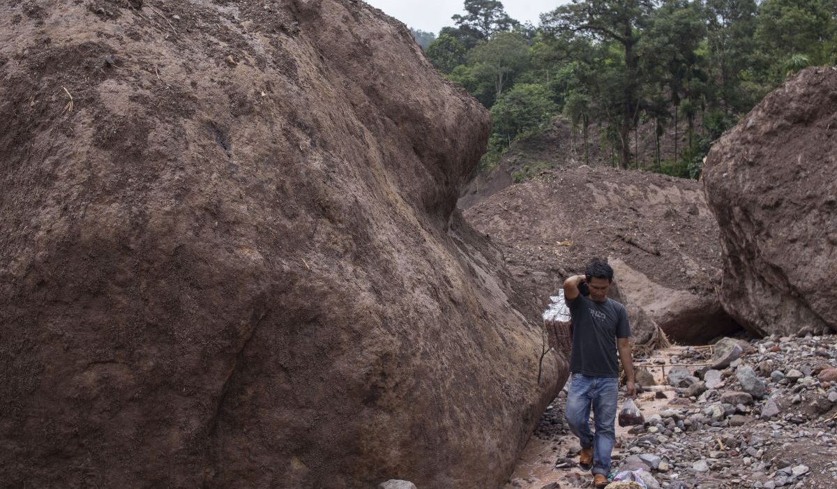 Warga berjalan di samping batu yang terbawa longsor di Langgai, Gantiang Mudiak Utara Surantiah, Kecamatan Sutera, Pesisir Selatan, Sumbar.