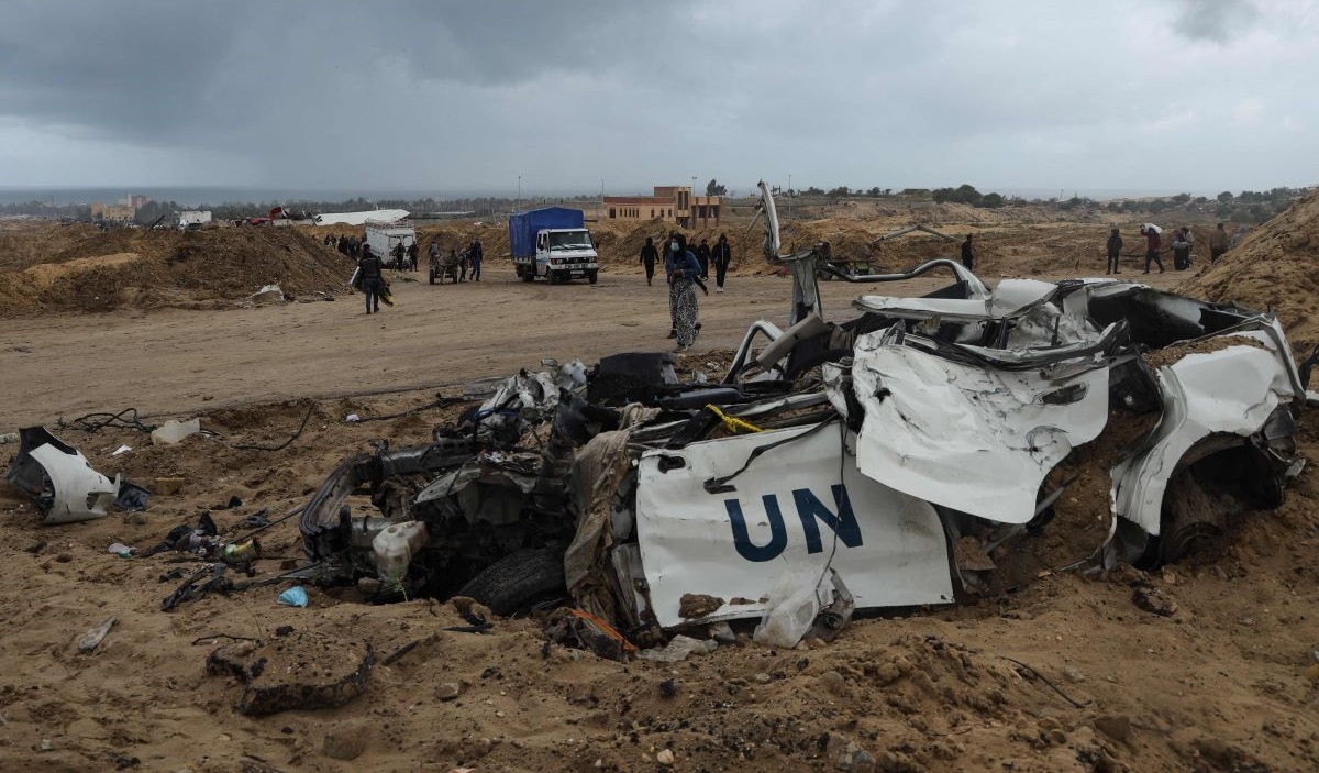 Warga Palestina berjalan melewati mobil PBB yang hancur di Khan Yunis, Jalur Gaza selatan.