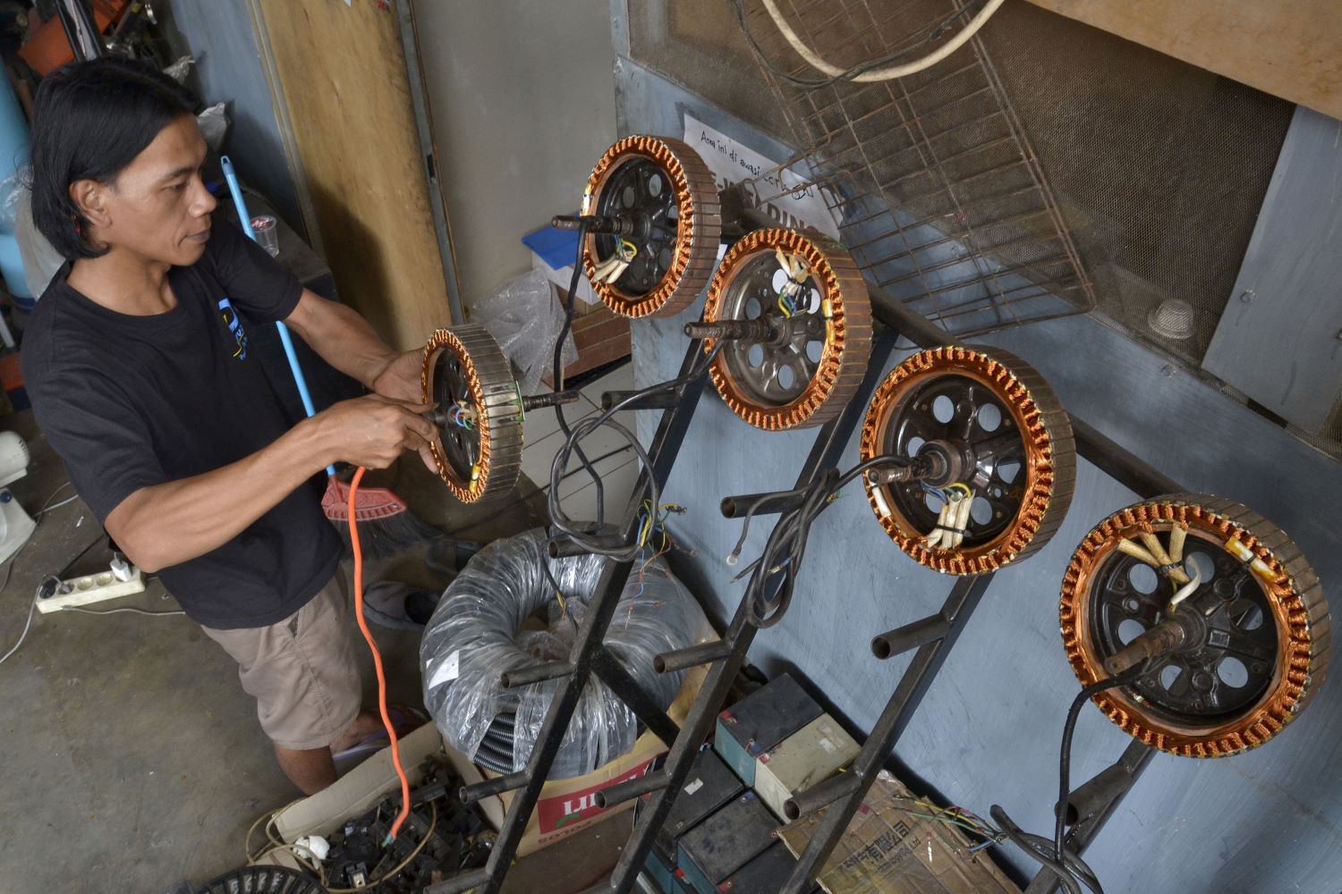 Seorang teknisi meletakkan dinamo motor listrik yang telah selesai dirakit di sebuah rak di bengkel motor listrik Bekasi. 