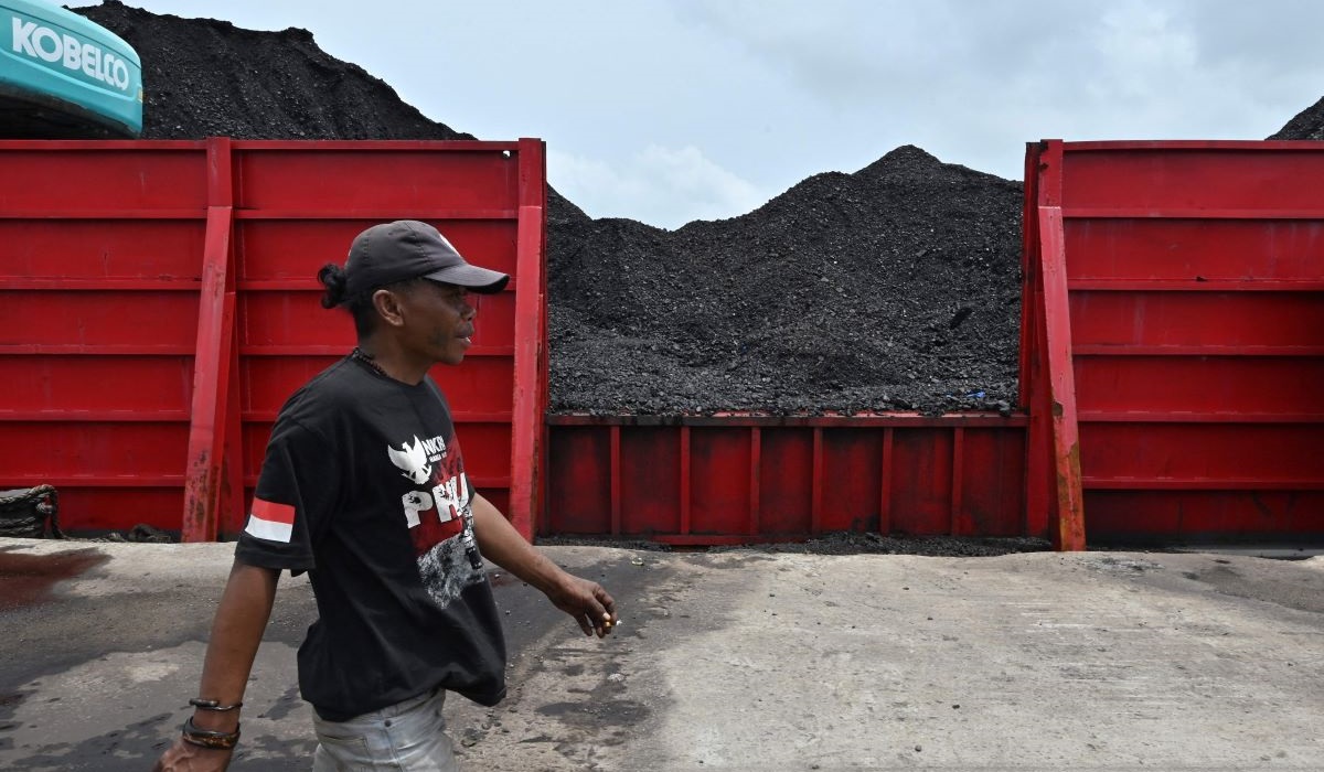 Seorang pria berjalan melewati tumpukan batu bara di pelabuhan Karya Citra Nusantara (KCN) Marunda di Jakarta pada 17 Januari 2022.