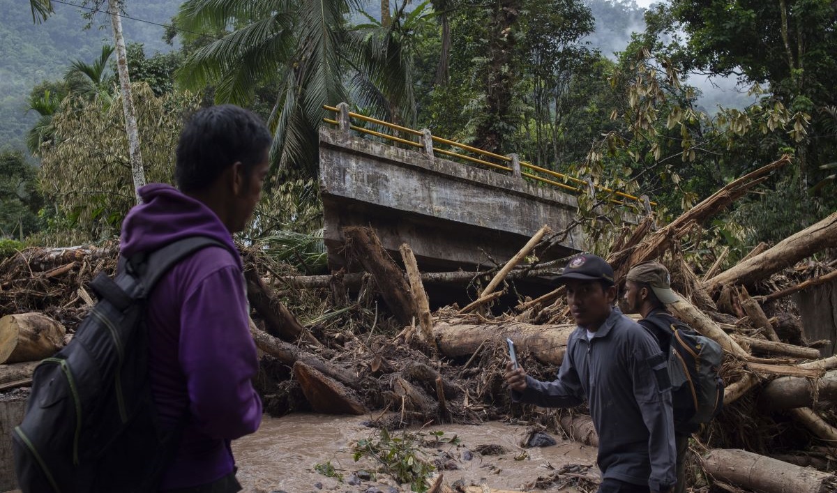 Warga melintas di dekat jembatan yang putus akibat banjir bandang di Langgai, Kecamatan Sutera, Pesisir Selatan.