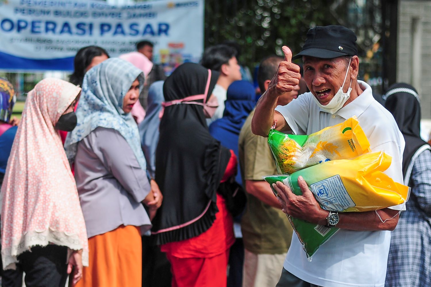 Warga mengacungkan jempol saat membawa beras yang dibeli saat operasi pasar.