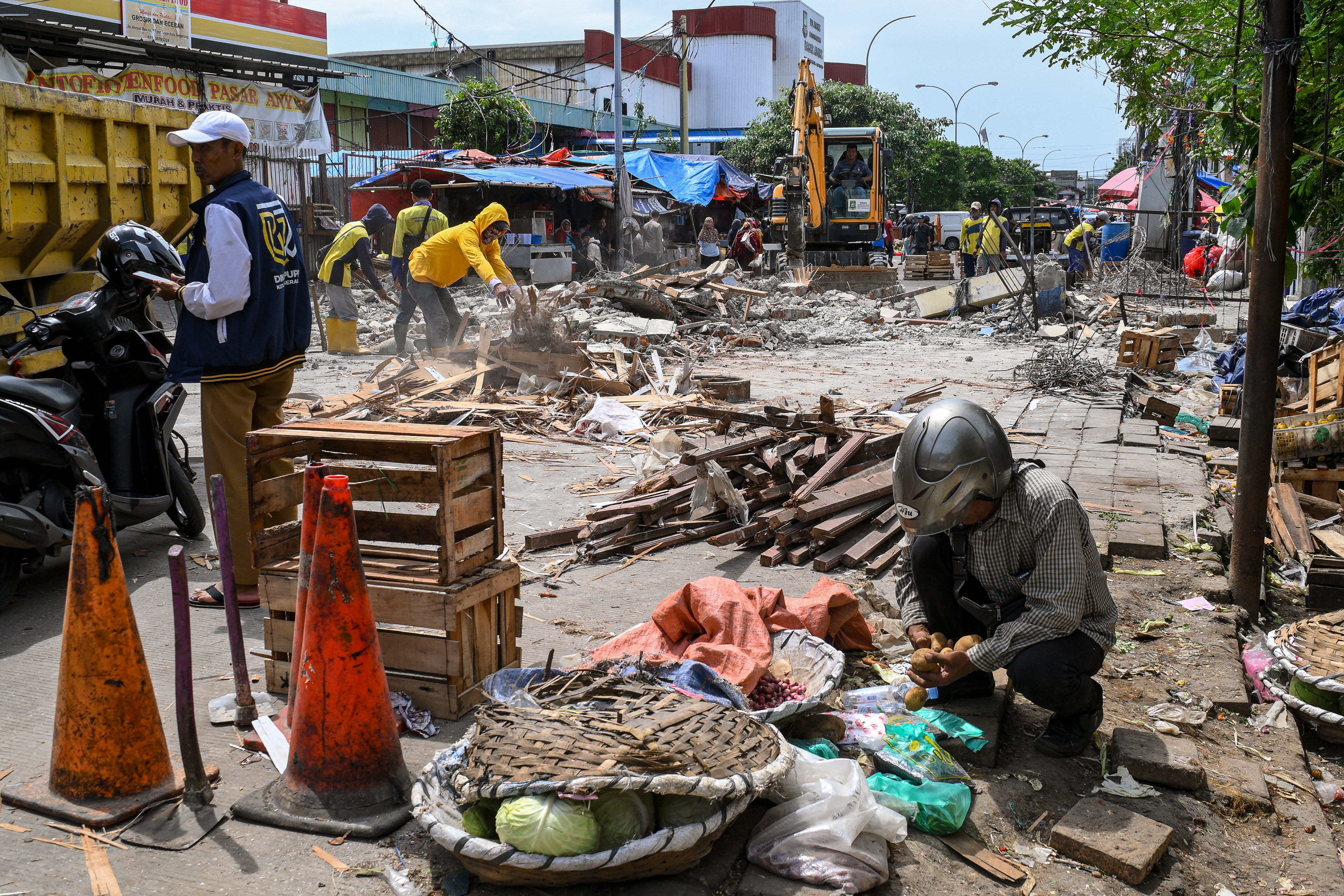 Seorang pedagang memindahkan barang dagangan dengan latar belakang petugas menggunakan alat berat membongkar gapura Pasar Anyar di Tangerang