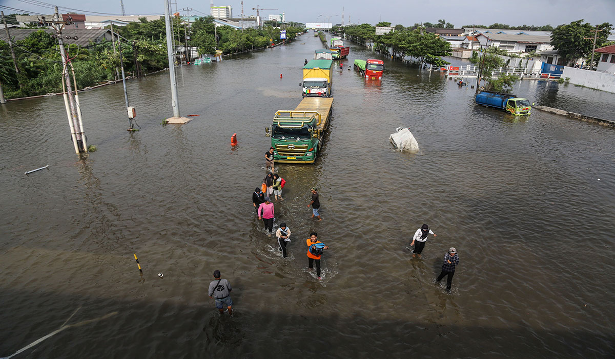 Warga melintas didekat truk yang berusaha menembus banjir di Jalur Pantura Kaligawe Raya-Genuk, Semarang, Jawa Tengah, Jumat (15/3).