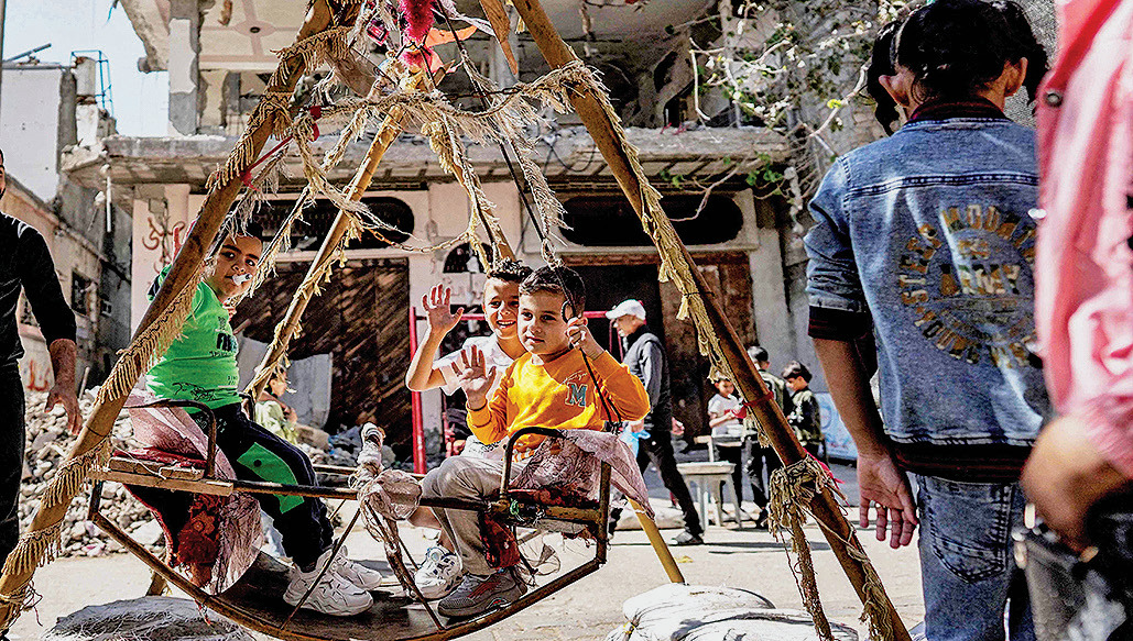 Anak-anak duduk di ayunan dengan latar gedung yang rusak akibat serangan militer Israel di Deir el-Balah, Jalur Gaza tengah, kemarin. 