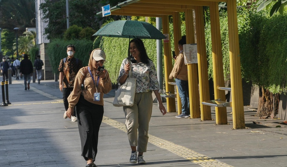 Warga berjalan menggunakan payung untuk melindungi dari panasnya sinar matahari di Jakarta.