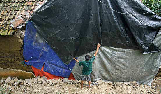Warga menutup tembok rumah yang roboh akibat terdampak oleh gempa dengan menggunakan terpal di Cipatat, Kabupaten Bandung Barat, Jawa Barat.