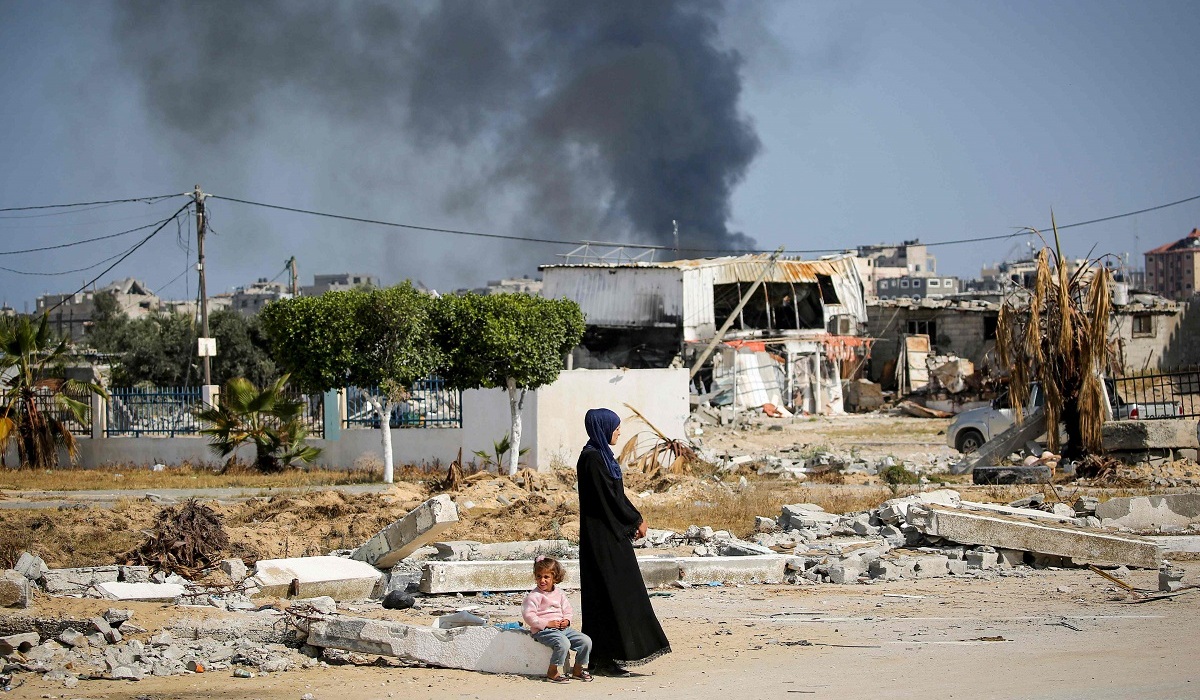 Asap mengepul ketika wanita dan anak-anak melihat di tengah puing-puing bangunan hancur akibat pemboman Israel di Khan Yunis, Jalur Gaza