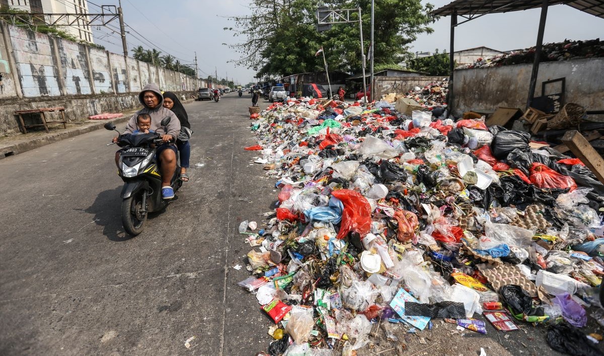 Warga melintas di samping sampah di Tempat Pembuangan Sampah Sementara (TPSS), Pancoran Mas, Depok, Jawa Barat, Rabu (12/7/2023).