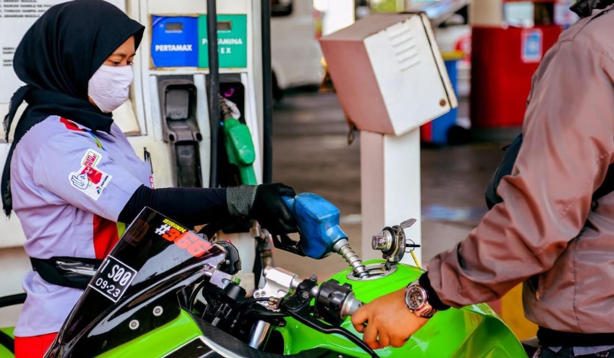 Petugas SPBU sedang melayani konsumen/pengendara sepeda motor.